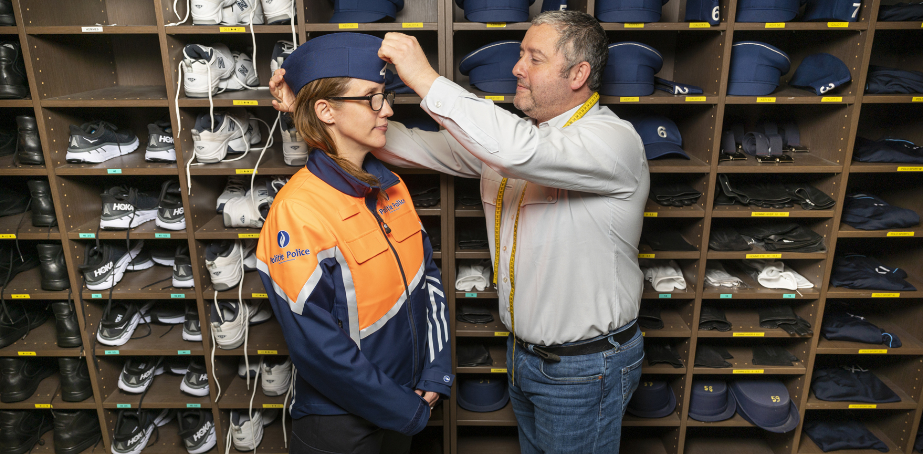 eine Frau probiert die Polizeiuniform an. Ein Mann setzt ihre Kopfbedeckung richtig.